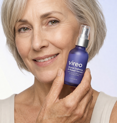 Light-skinned mature woman holding Vireo Bruise Defense & Repair Serum